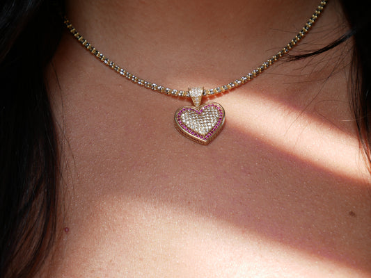 A 14k gold heart-shaped pendant encrusted with small clear gemstones and outlined with pink stones. The pendant features a sparkling design, giving a luxurious and elegant appearance.