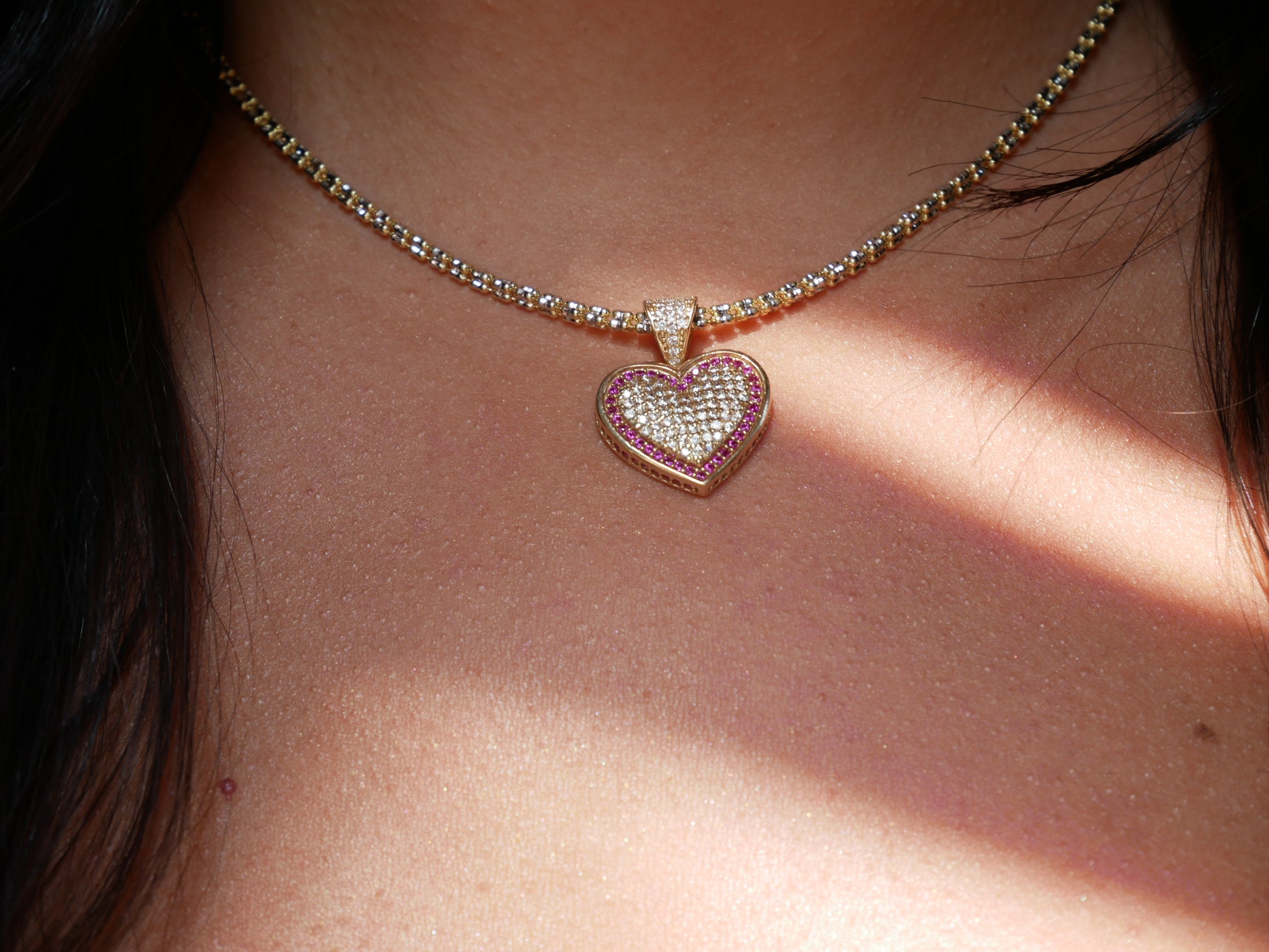 A 14k gold heart-shaped pendant encrusted with small clear gemstones and outlined with pink stones. The pendant features a sparkling design, giving a luxurious and elegant appearance.
