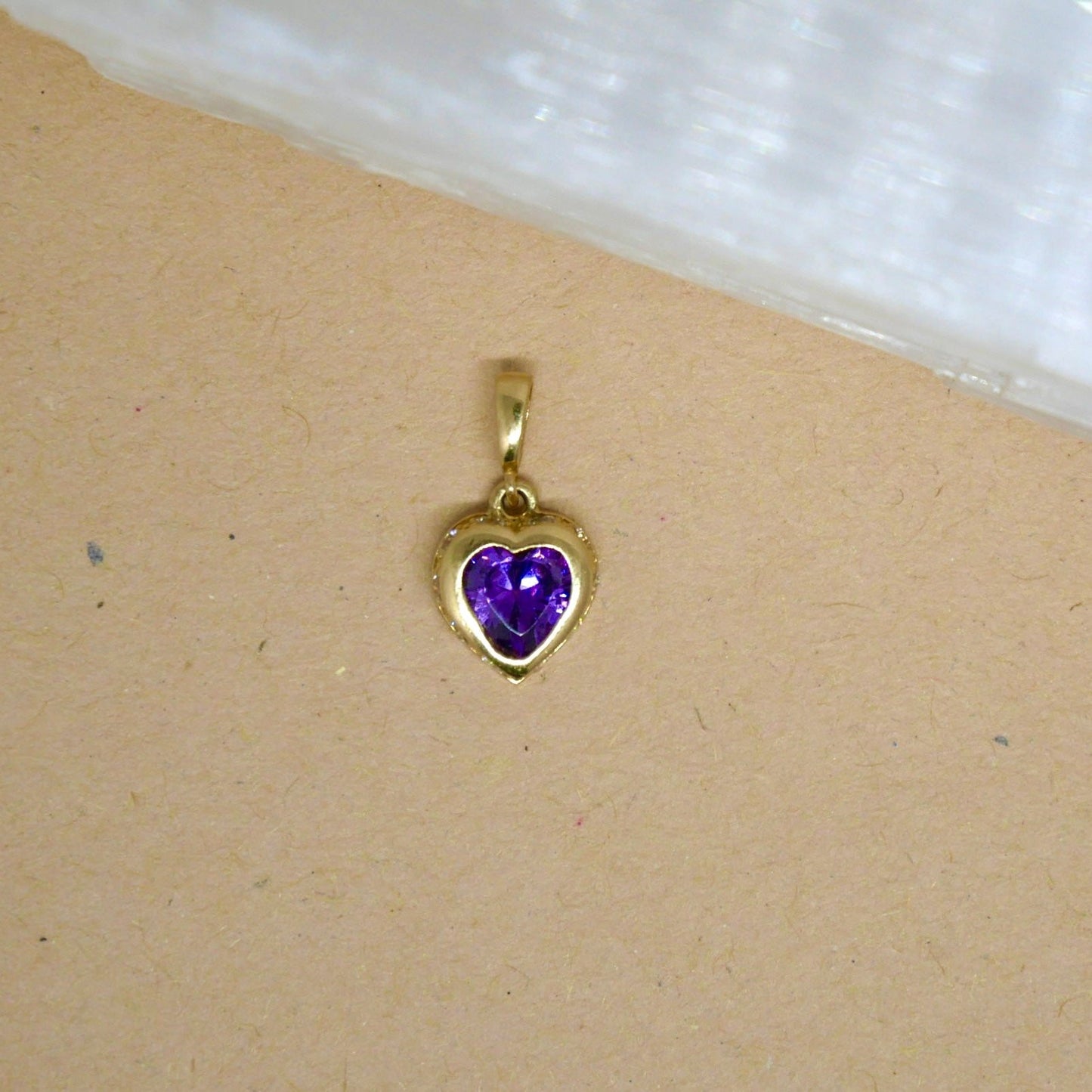 14k solid gold heart-shaped pendant featuring a vibrant purple gemstone set in a smooth gold bezel, offering a beautiful contrast of color and elegance.