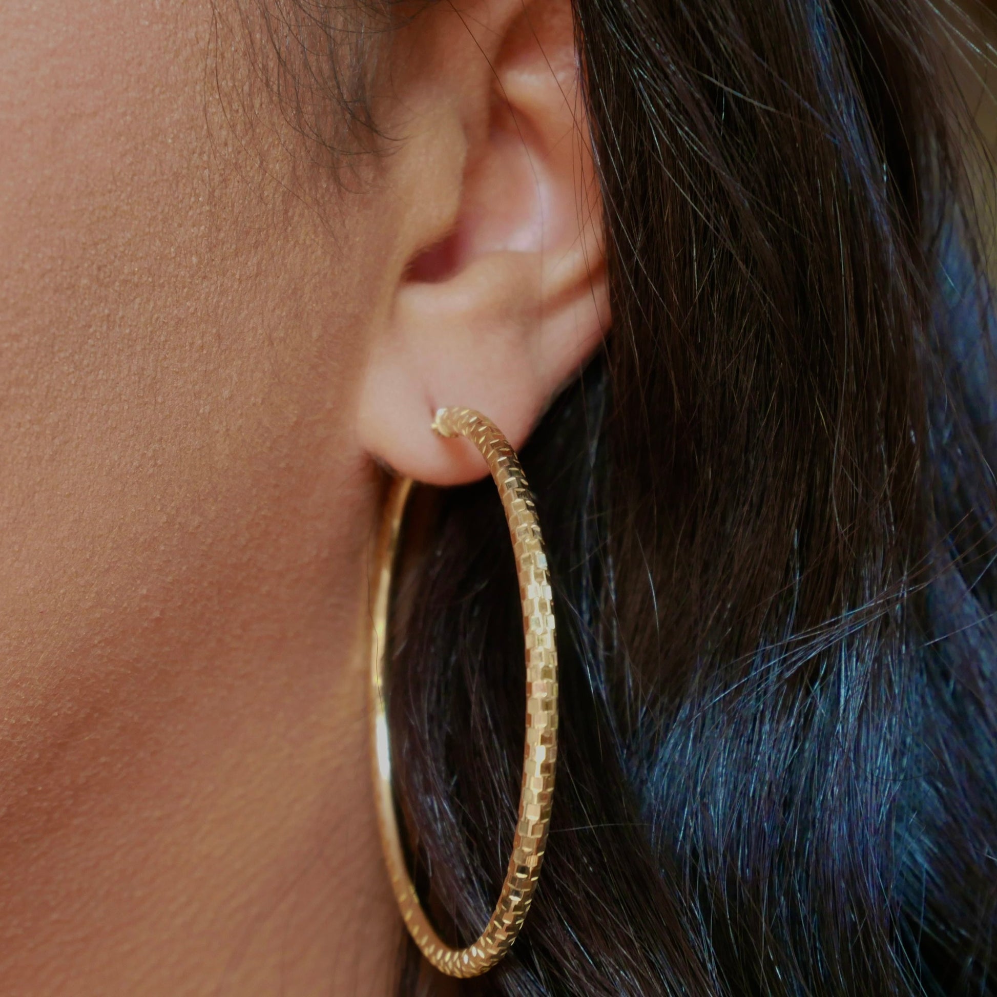 A pair of 14k solid gold hoop earrings with a faceted texture, displayed on a neutral background, showcasing their polished finish and elegant, lightweight design.