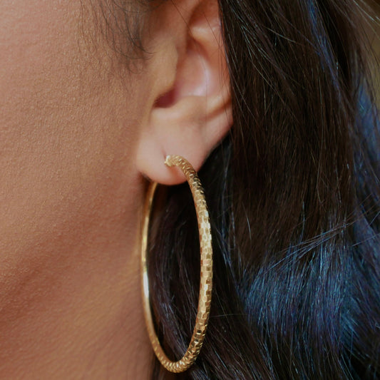 A pair of 14k solid gold hoop earrings with a faceted texture, displayed on a neutral background, showcasing their polished finish and elegant, lightweight design.