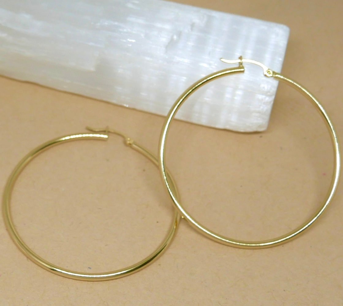 14k solid yellow gold large high-polished hoop earrings, 50mm diameter x 2mm width, featuring a sleek finish with a secure latch-back closure.