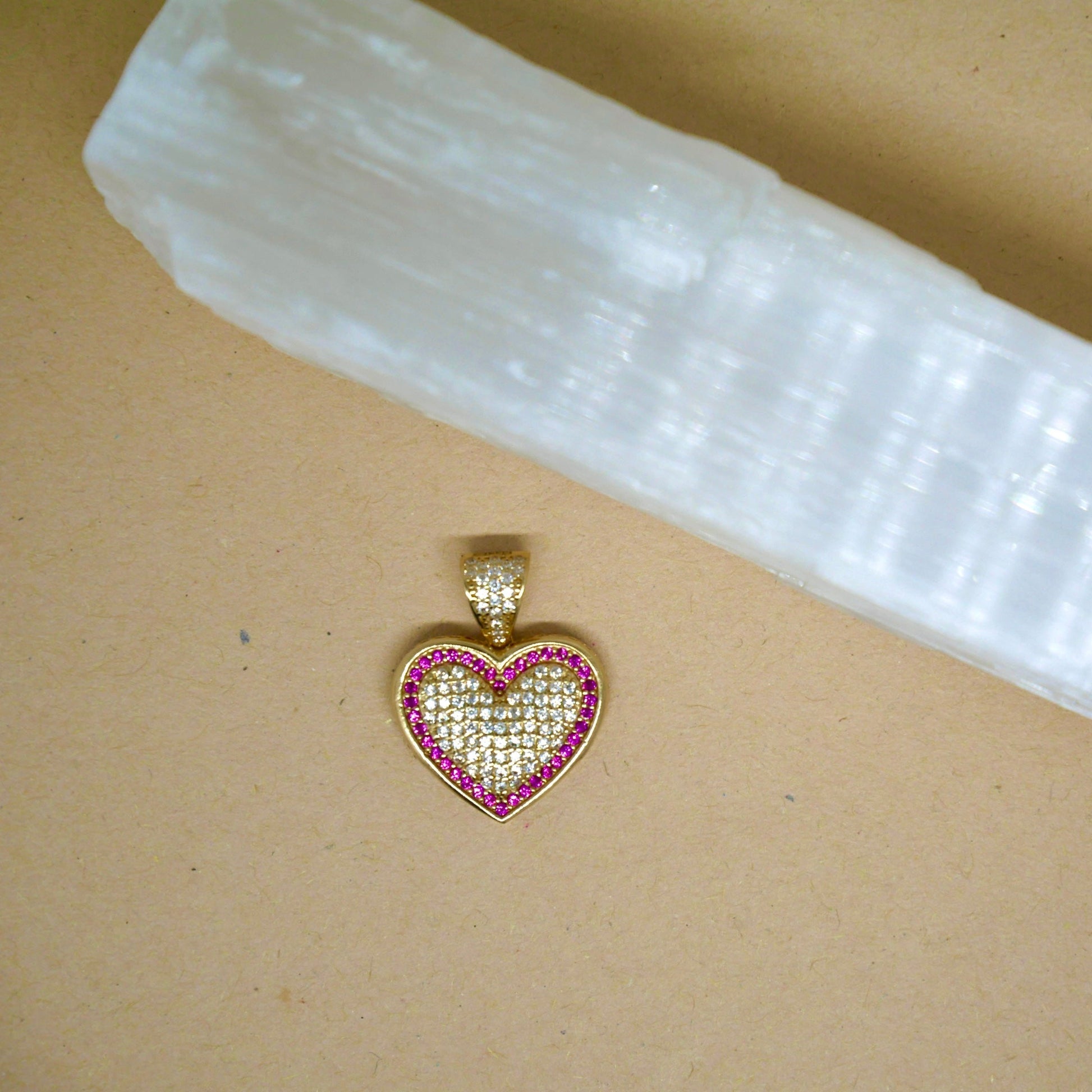 A 14k gold heart-shaped pendant encrusted with small clear gemstones and outlined with pink stones. The pendant features a sparkling design, giving a luxurious and elegant appearance.
