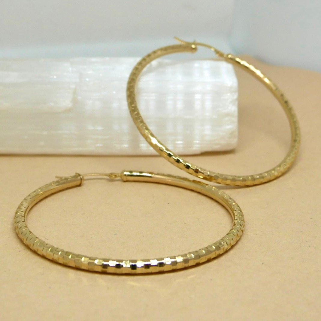 A pair of 14k solid gold hoop earrings with a faceted texture, displayed on a neutral background, showcasing their polished finish and elegant, lightweight design.