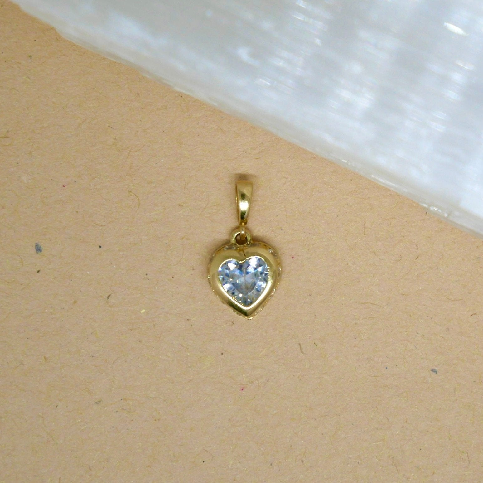 14k solid gold heart-shaped pendant featuring a vibrant white gemstone set in a smooth gold bezel, offering a beautiful contrast of color and elegance.